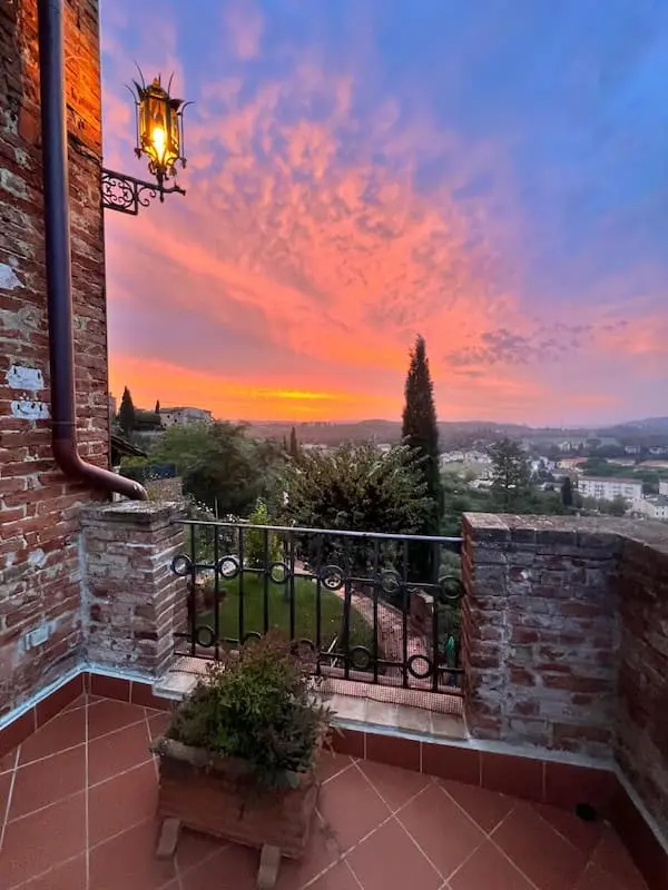 Sunset view from a terrace in Certaldo Alto overlooking the town of Certaldo, with garden, brick walls and colorful evening sky.