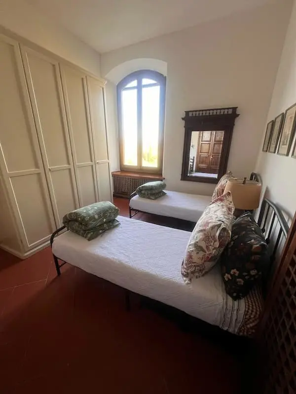 Twin bedroom in the house in Certaldo Alto with two single beds, wardrobe and an arched window providing natural light.