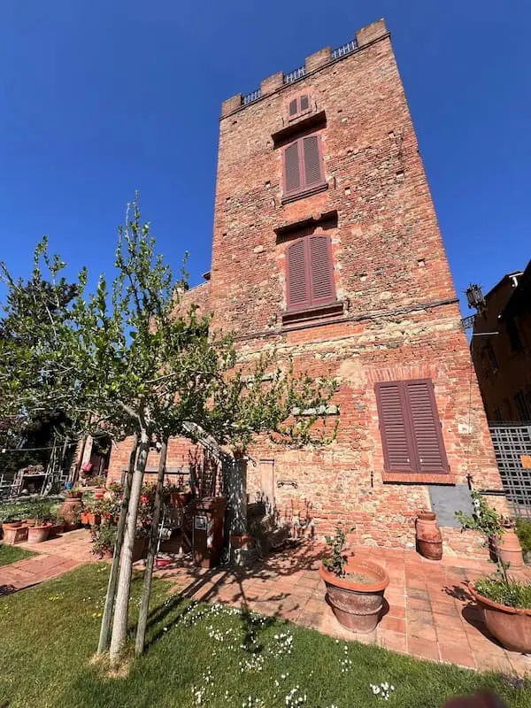 Historic brick house with a medieval tower and garden in Certaldo Alto, surrounded by traditional architecture and greenery.