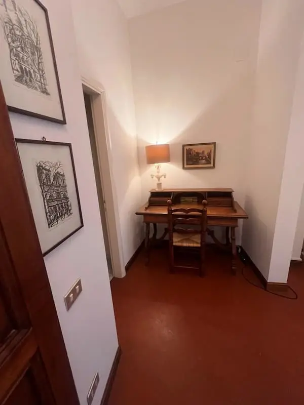 Small study corner with a wooden writing desk, chair and lamp inside the house in Certaldo Alto.