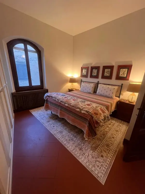 Double bedroom in the house in Certaldo Alto with a double bed, bedside lamps, arched window and traditional furnishings.
