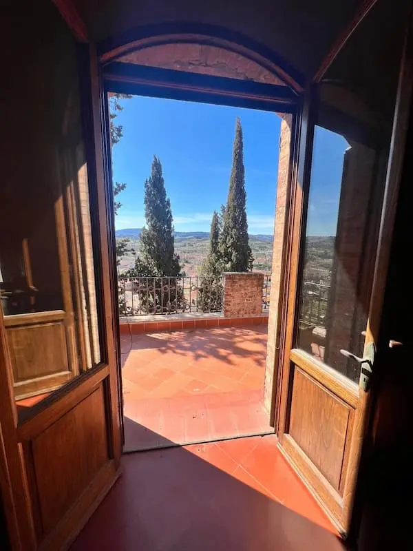 View through arched wooden doors from inside the house in Certaldo Alto onto the terrace with cypress trees and views over Certaldo.