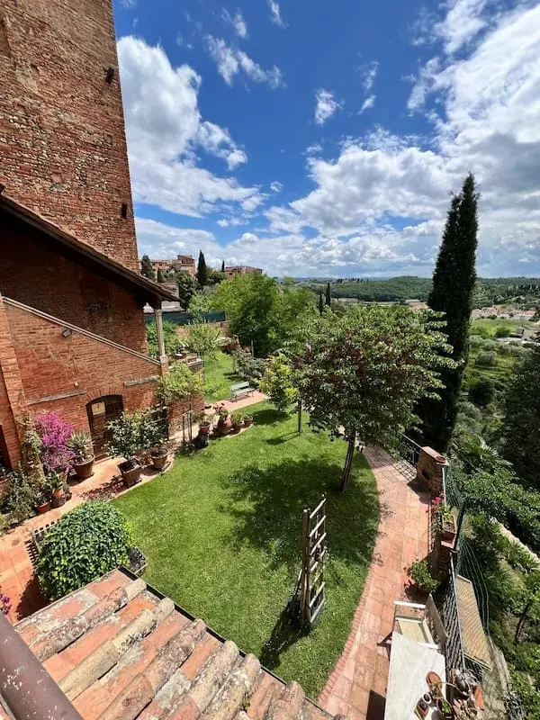 Garden next to the house overlooking green hills, trees and village rooftops under a bright blue sky