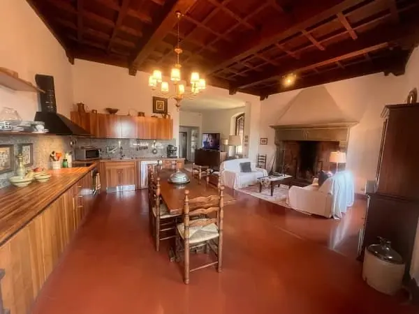 Open‑plan kitchen, dining and living area in the house in Certaldo Alto with historic fireplace, wooden beams and traditional furnishings.